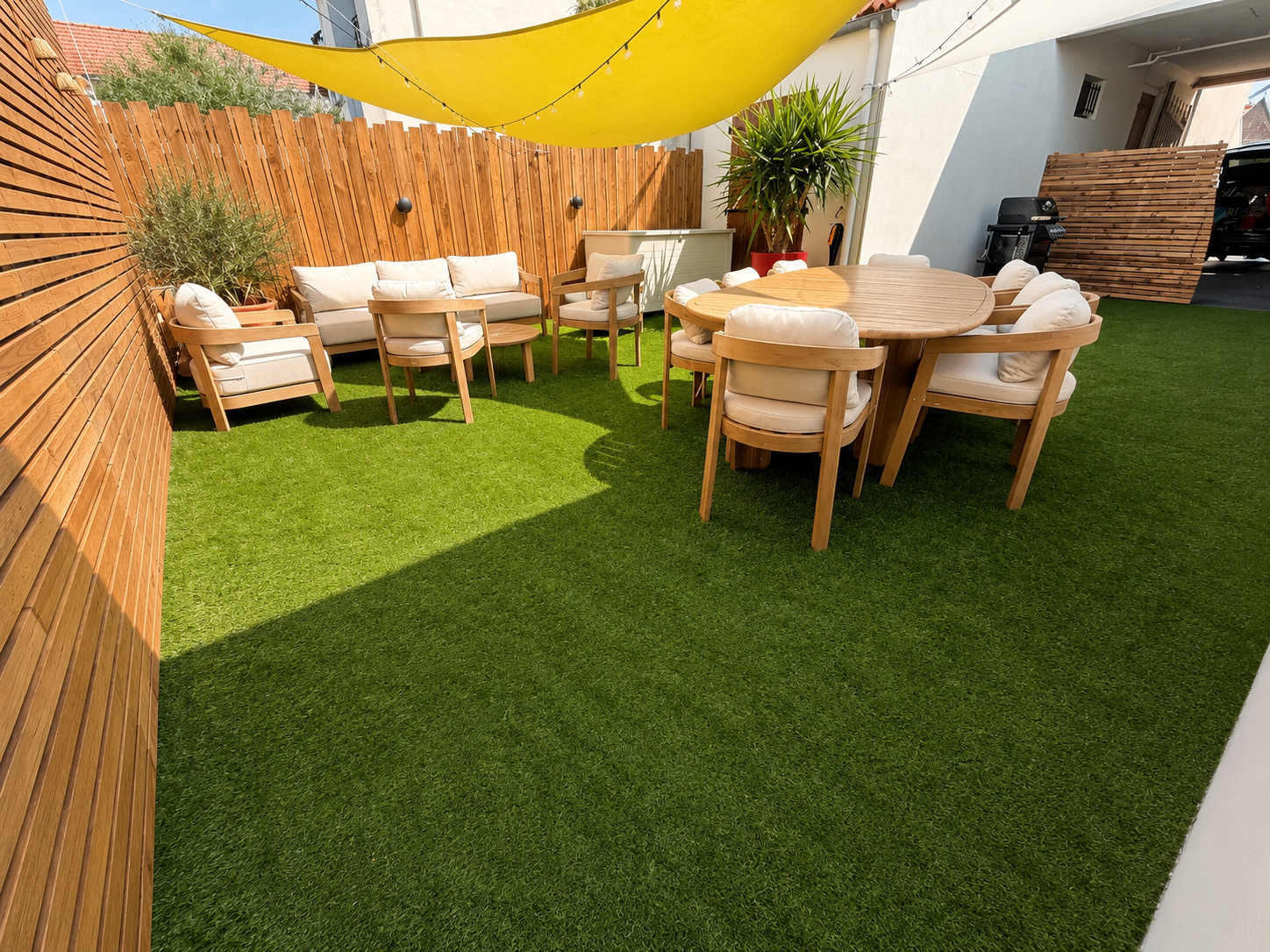 Patio avec voile d'ombrage jaune, salon et table à manger en teck sur gazon