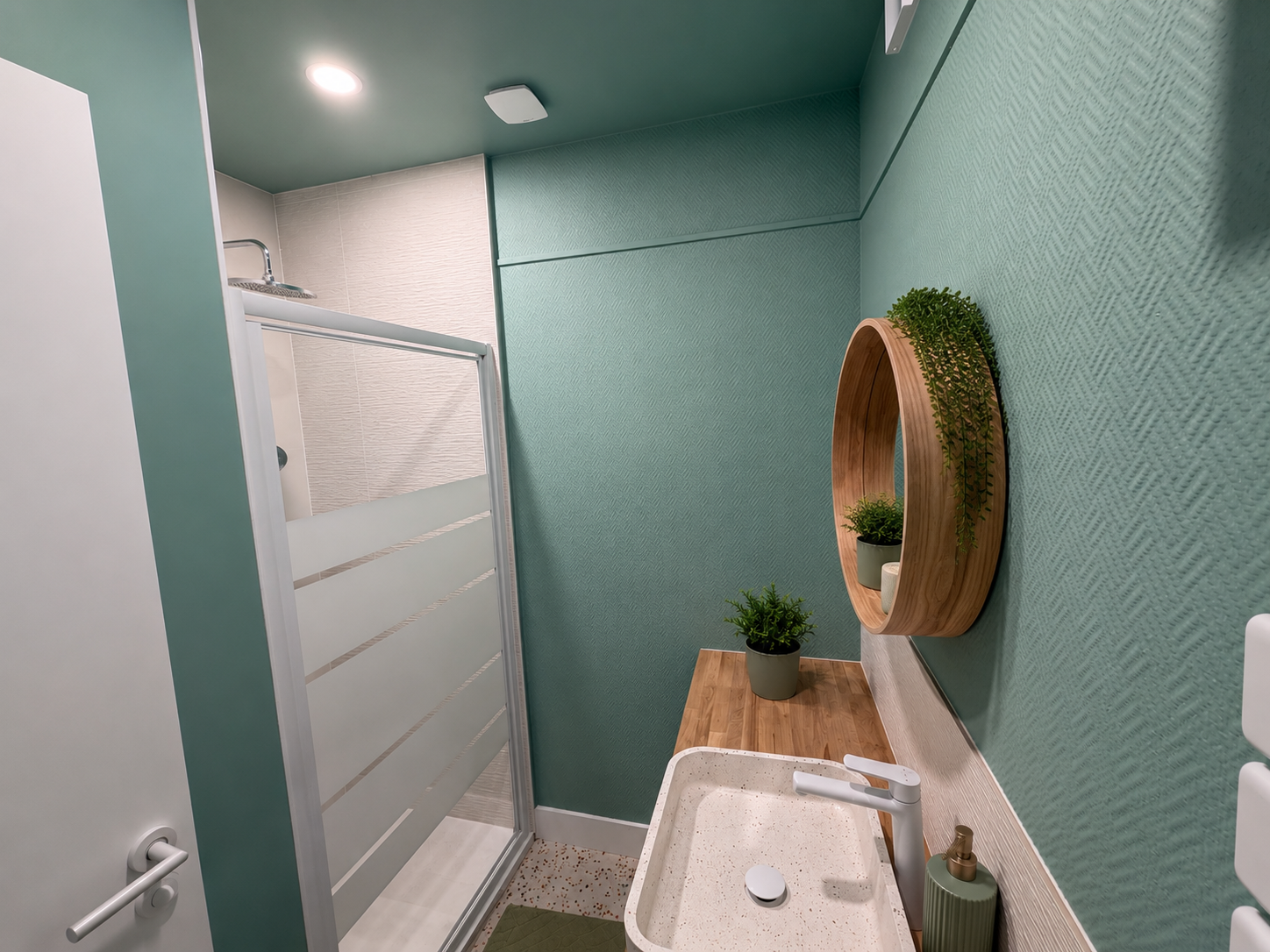 Salle d'eau verte avec vasque terrazzo, miroir rond et douche